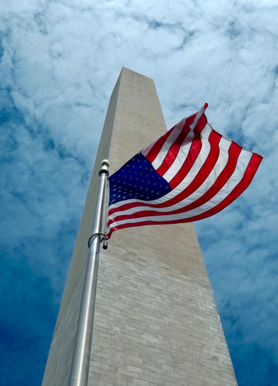low angle shot of the american flag and the washington monument in washington d c