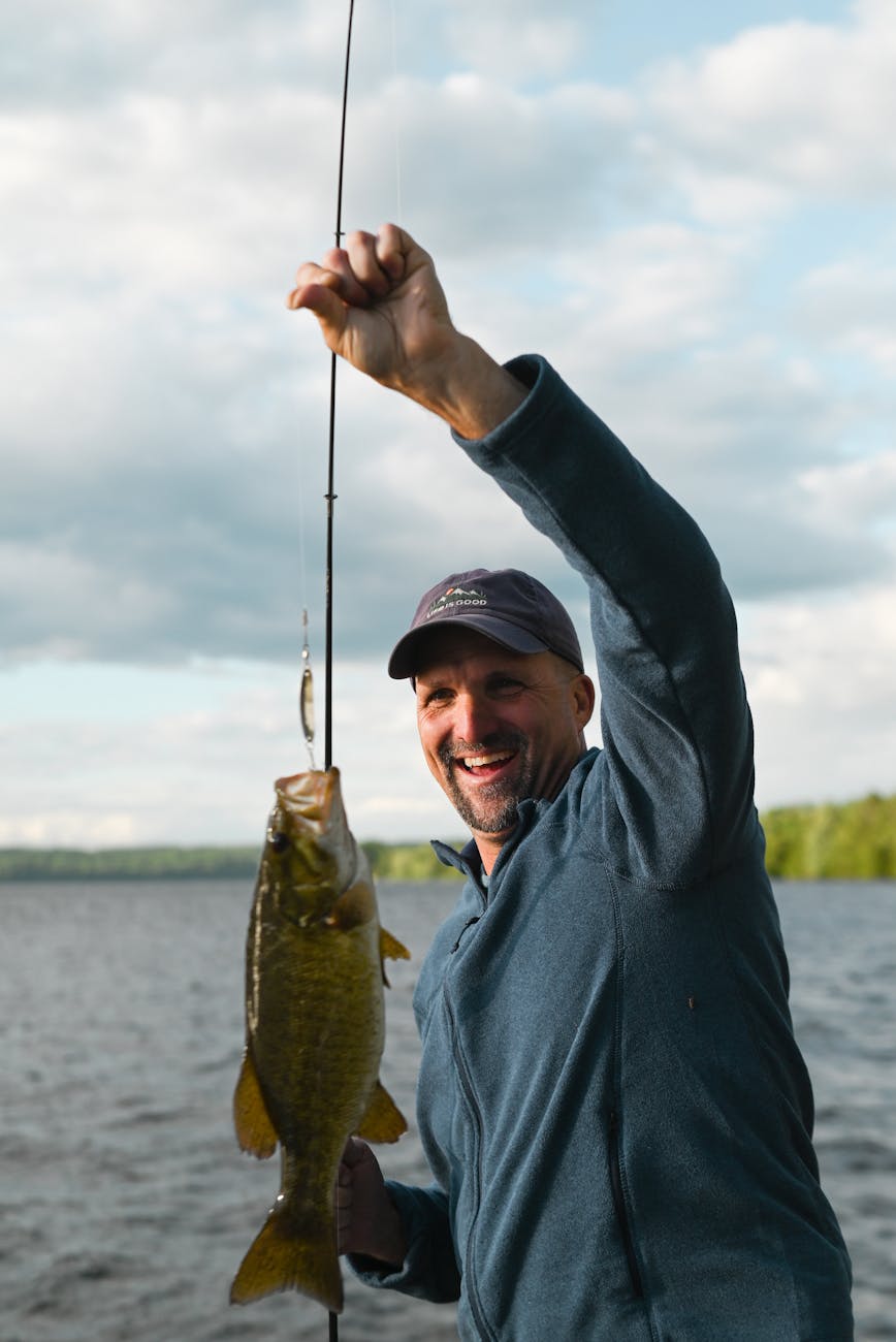 man smiling in blue jacket catching a fish